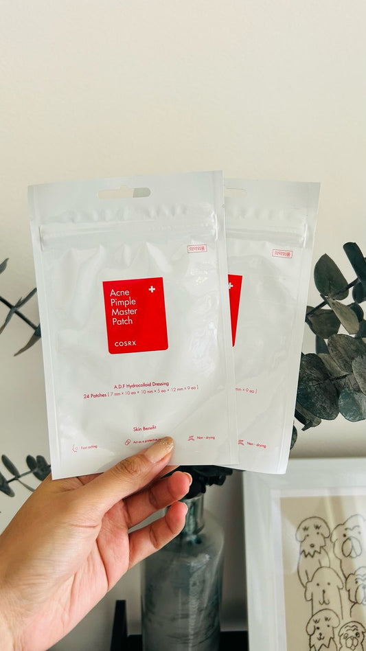 Una mano sostiene dos paquetes de parches Bemba. COSRX Acne Pimple Master Patch sobre un fondo verde y un jarrón con un bonito dibujo. Ideales para el cuidado del acné, promueven la cicatrización y reducen la inflamación.