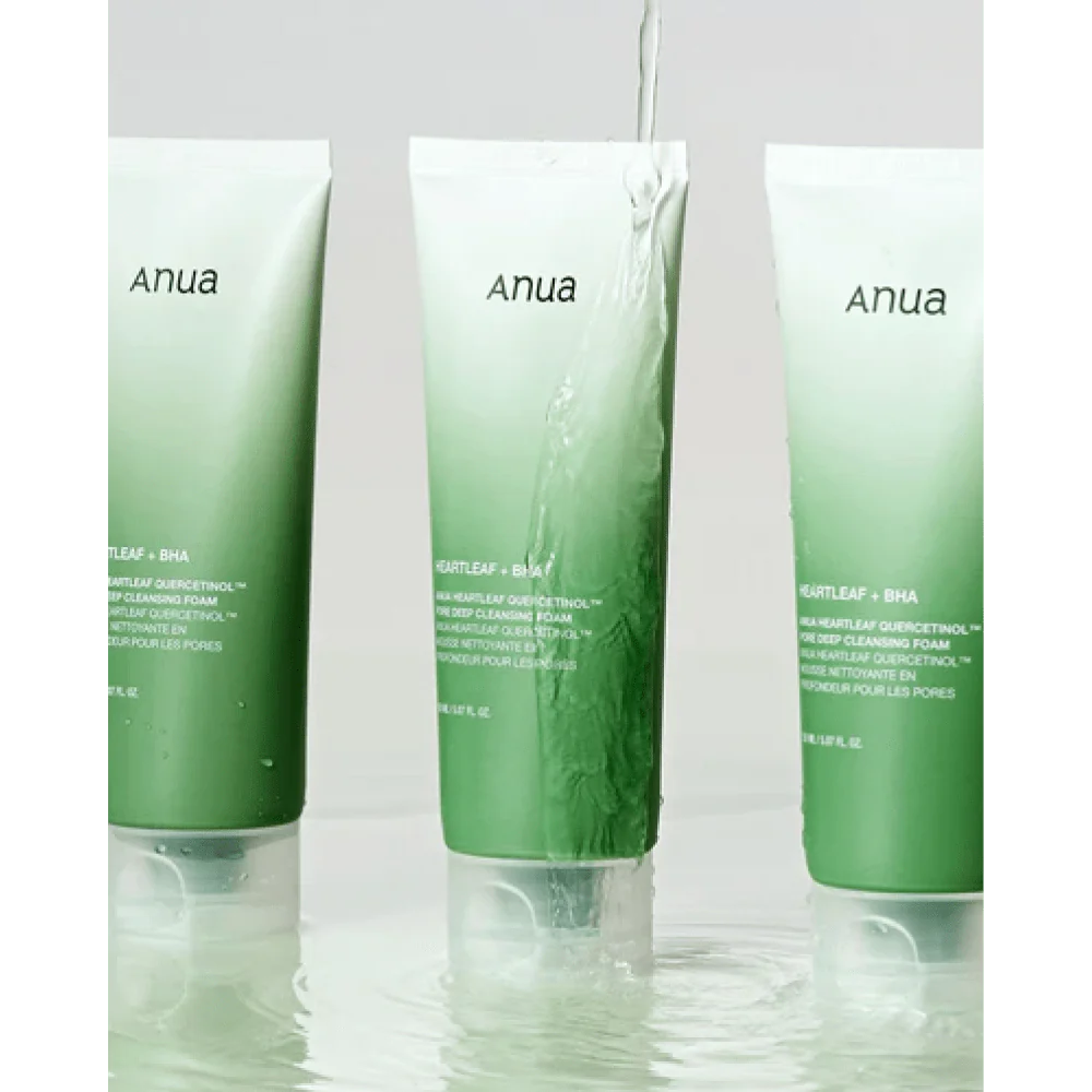 Tres tubos verdes degradados, etiquetados como Bemba, se encuentran en posición vertical en agua poco profunda, con un chorro que vierte sobre el tubo central. Esta es la Espuma Limpiadora Profunda de Poros con Quercetinol Anua Heartleaf, un limpiador diseñado para purificar y refrescar la piel en profundidad.